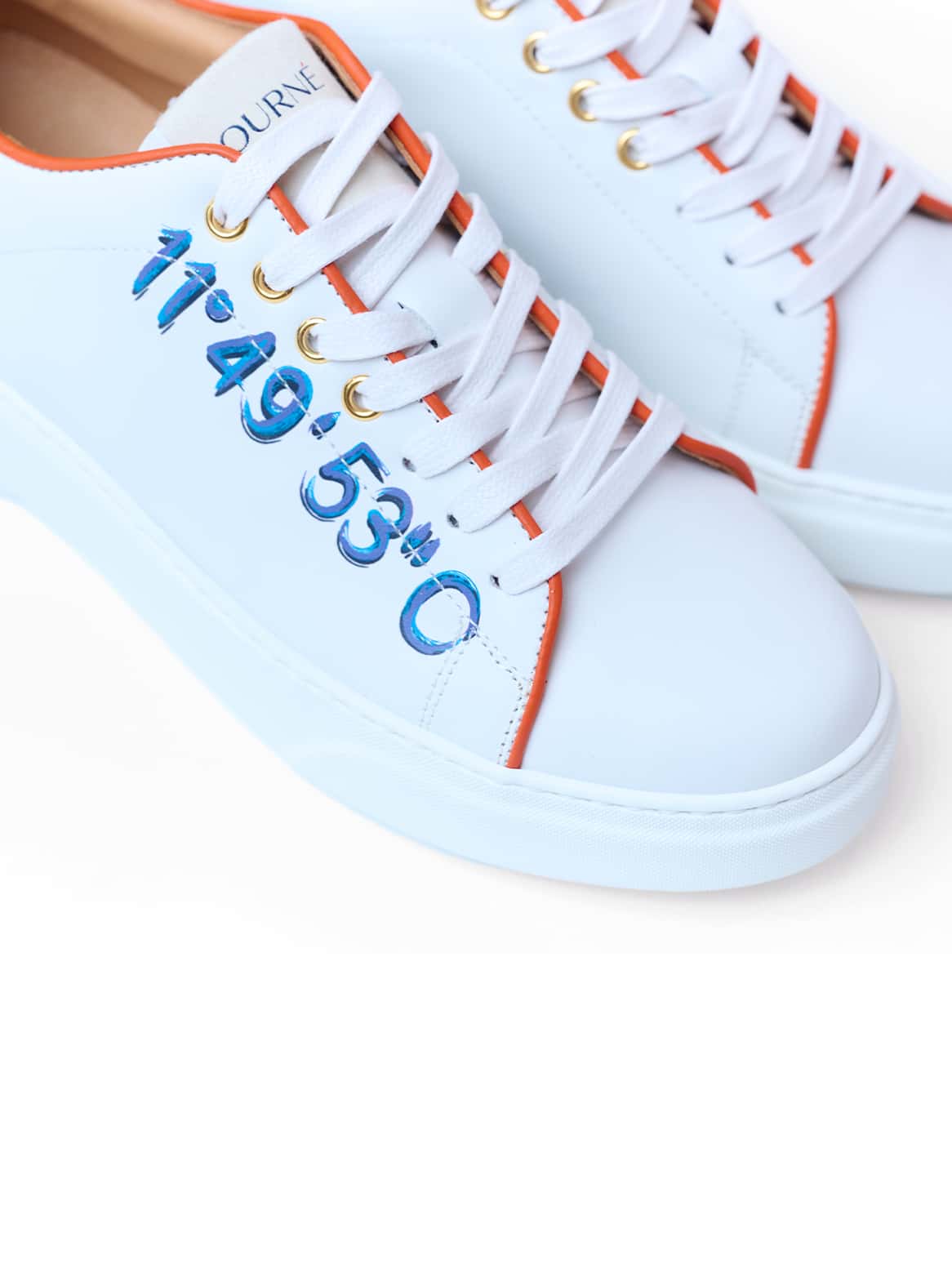 Petra Sneaker am Fuß – mit auffälliger blauer Koordinatenprägung und orangen Akzenten
